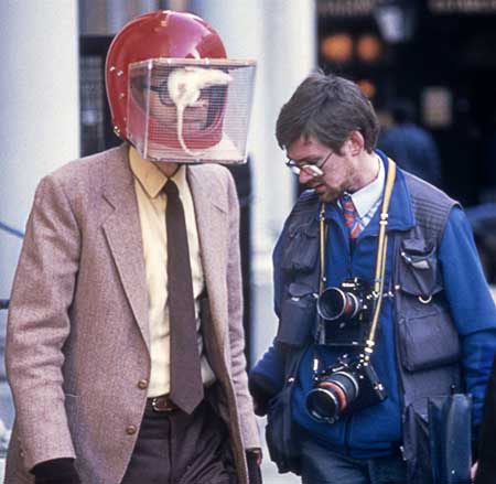 Colour photograph of a photojournalist and Rick Gibson wearing the rat helmet