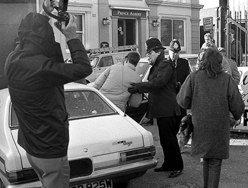 Rick Gibson being put into the back of a police car by the senior police officer