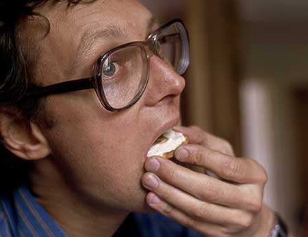 Colour photo of Gibson holding human tonsil hors d'oeuvre half-way inside his mouth
