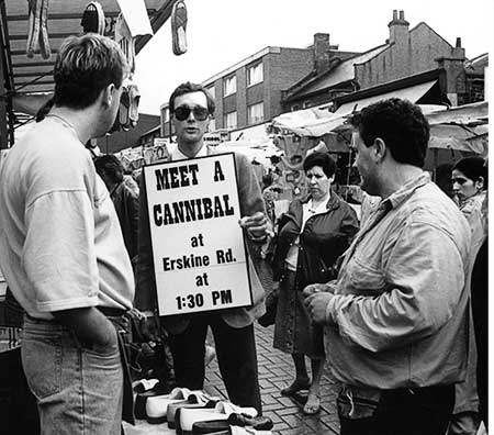 Black and white photo of Gibson talking with shoppers and merchants about cannibalism