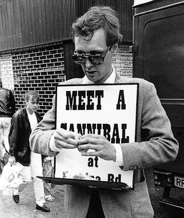 Black and white photo of Gibson making the human tonsil hors d'oeuvre on a shelf attached to his sign