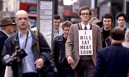 Color photo of Gibson wearing a sign reading "I will eat meat soon" walking with journalists and supporters