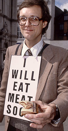 Color photo of Gibson showing photographers the remaining half of the meat hors d'oeuvre