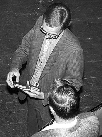 Black and white photo of Gibson searching for his identification card while a police detective looks on