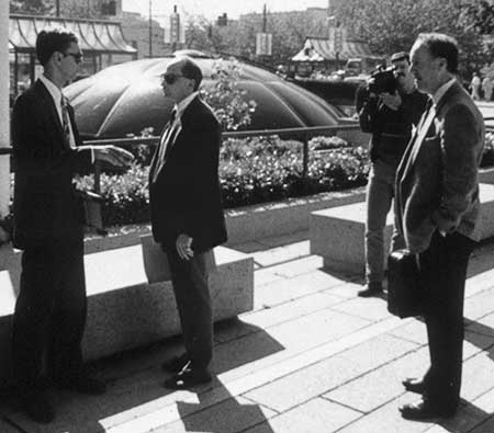 Black and white photo of Gibson talking to the lead detective, a police videographer and another police detective