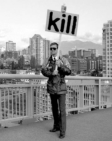 Black and white photo of Gibson walking across the Granville Street bridge carrying a sign reading "Kill"