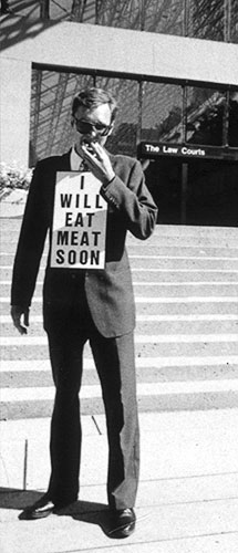 PICTURE: black and white photo of Gibson eating the meat hors d'oeuvre on the steps of the Vancouver Law Courts.
