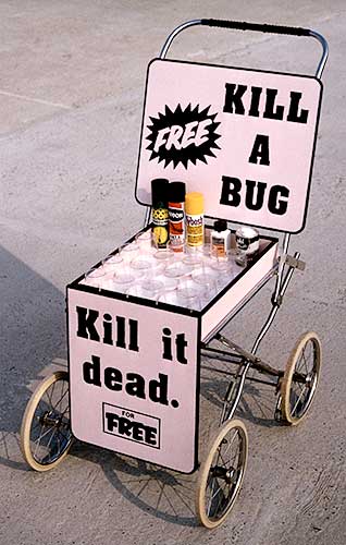 PICTURE: color photo of a converted baby buggy (pram) with two signs.  One sign reads - Free Kill a Bug - and the other sign reads - Kill it dead for free. In the middle is a box containing 16 clear plastic cups and an assortment of insect poison powders and sprays.  The main colors of the pram and signs is black and pink
