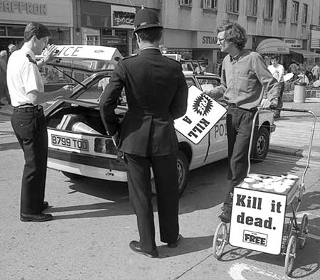 PICTURE: black and white photo of Gibson dismantling his display and the police putting it in the boot (trunck) of a police car.