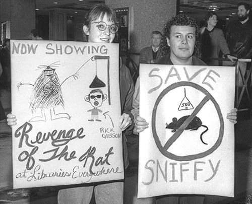 PICTURE: black and white photo of two protesters holding signs in the lobby of the Hotel Vancouver.  The sign on the left reads - Now Showing Revenge of the Rat at Libraries everywhere - and the other sign on the right reads - Save Sniffy.